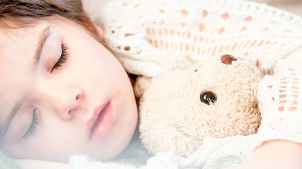 child sleeping in bed with teddy bear