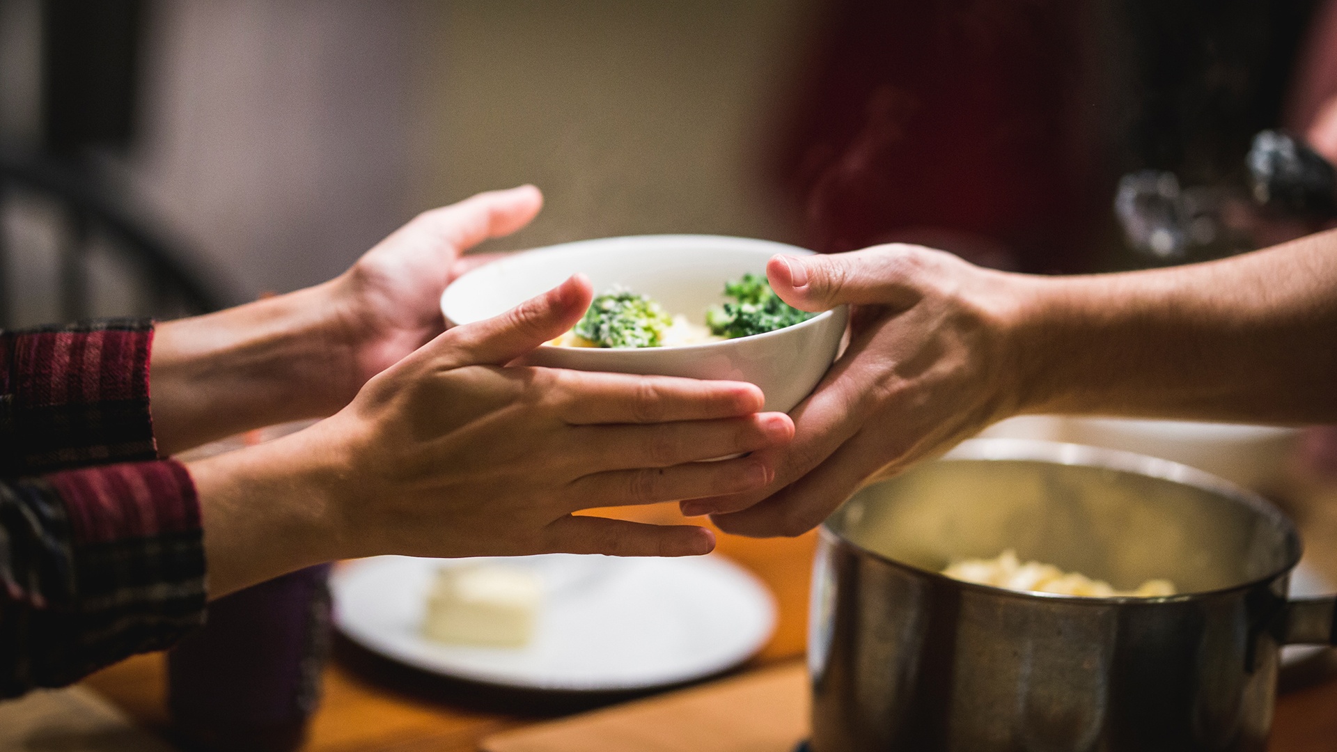 Close up of hand passing a bowl of food to another pair of hands.