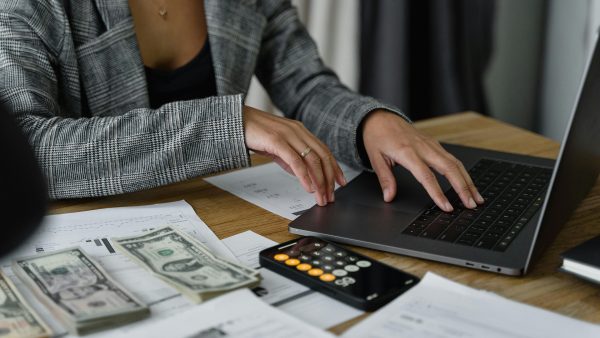 Woman with her hands on a computer, and money and a calculator nearby