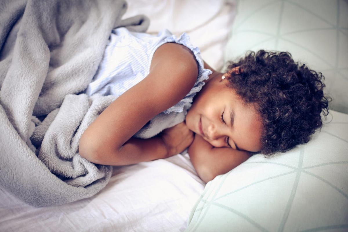 Girl cuddled under blanket in bed